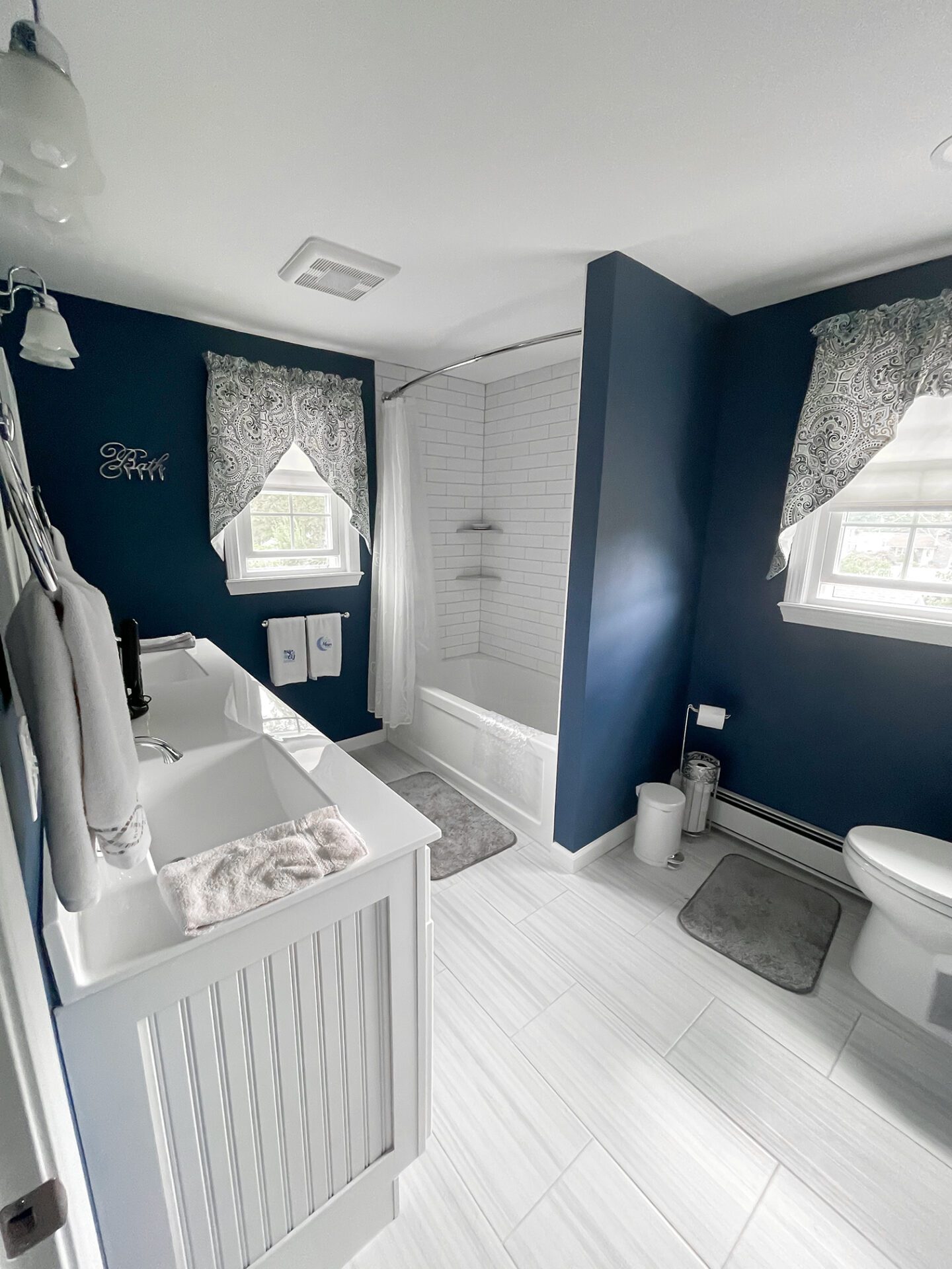 481160082_1345913776851468_6543473262678523116_n Stylish bathroom remodel in Newington, CT featuring white wood-paneled vanity, navy blue walls, subway tile shower surround, and modern white tile flooring with soft gray accents.