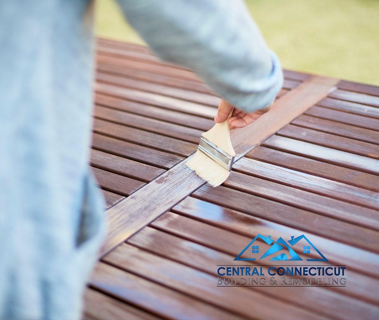 Deck Build in Newington Close-up of a hand using a brush to apply protective stain to a wooden deck surface — Central Connecticut Building & Remodeling preserving and finishing a deck in Newington, CT.